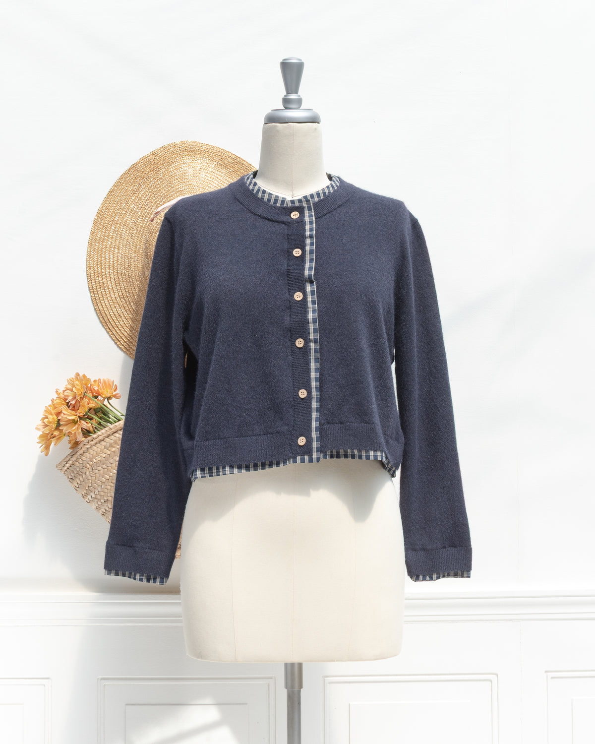 Navy knit cropped cardigan with plaid trim and wood tone buttons, a classic wardrobe staple, mannequin front view.
