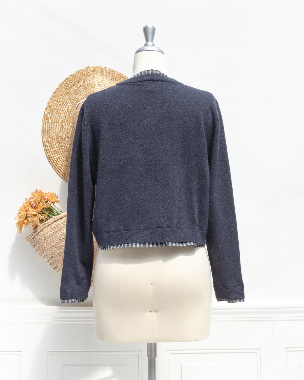 Navy knit cropped cardigan with plaid trim at the hem and cuffs, a feminine fall layer, mannequin back view.