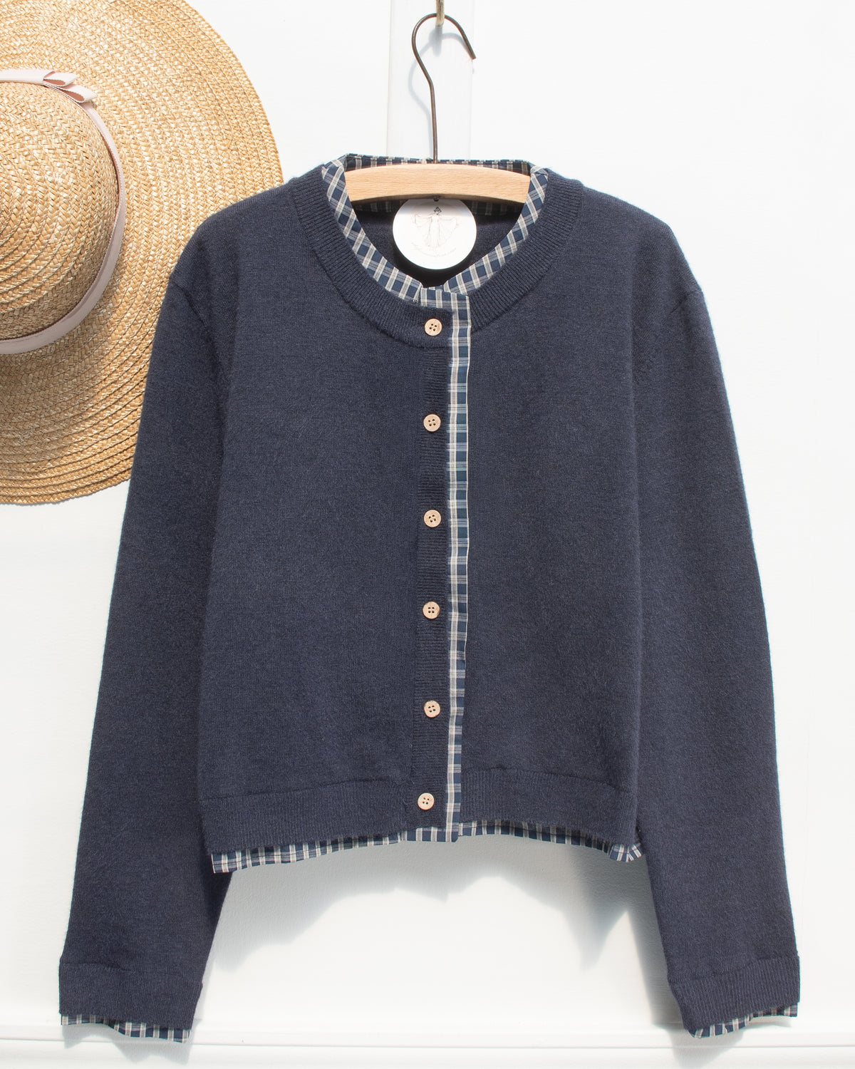 Navy knit cropped cardigan with plaid collar and ribbed hem shown on a hanger, front view.