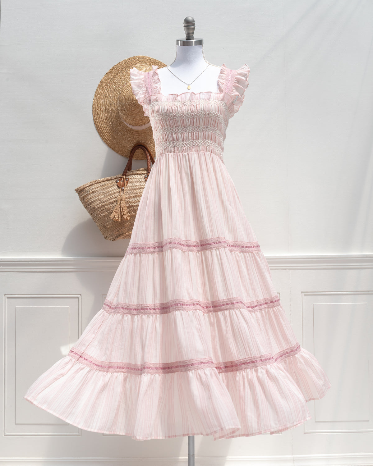 Blush pink striped midi dress with smocked bodice and tiered skirt on a mannequin, romantic French girl style, front view.