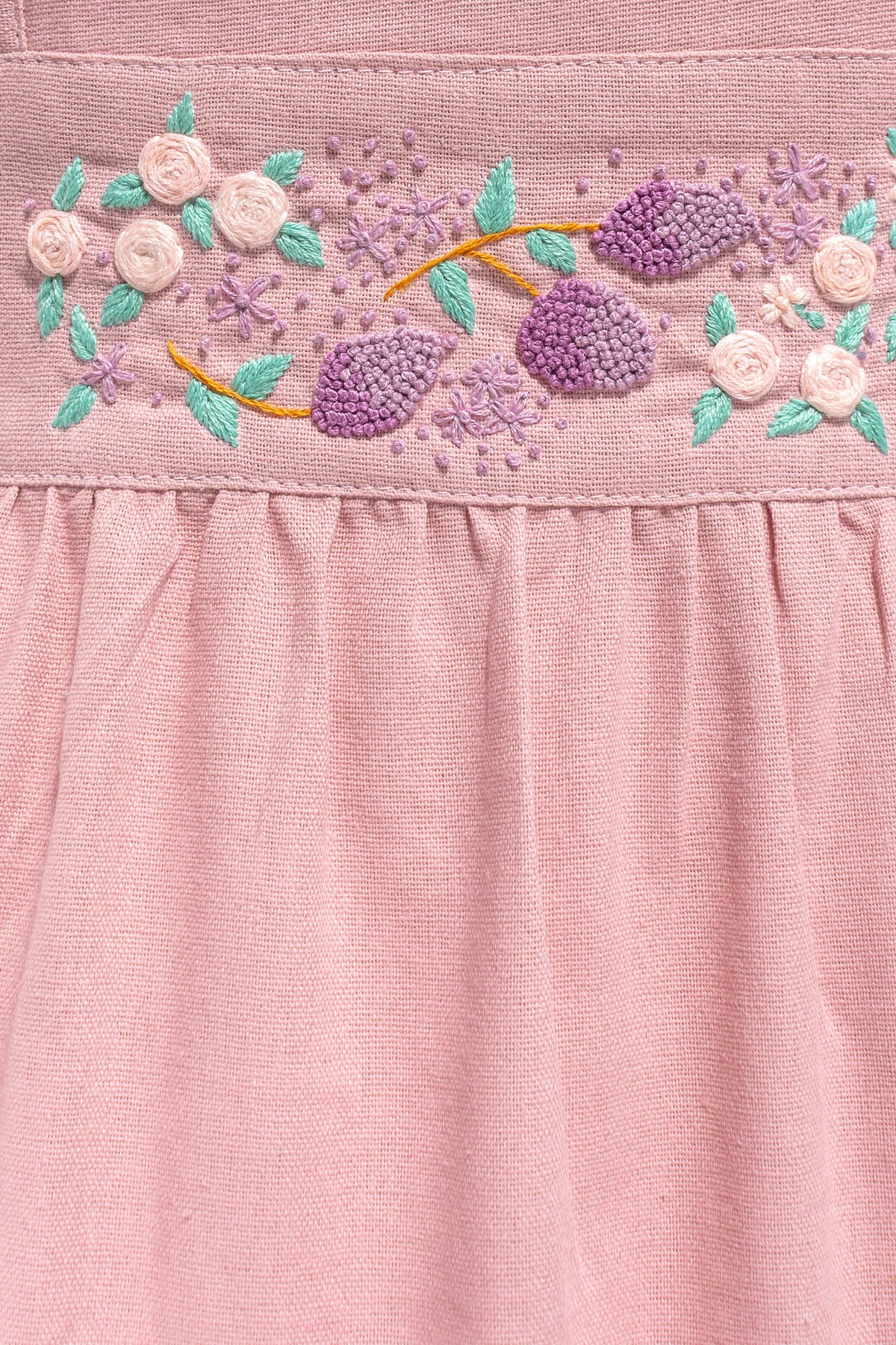 Close up of hand embroidered waistband with roses lavender and green leaves on pink apron.
