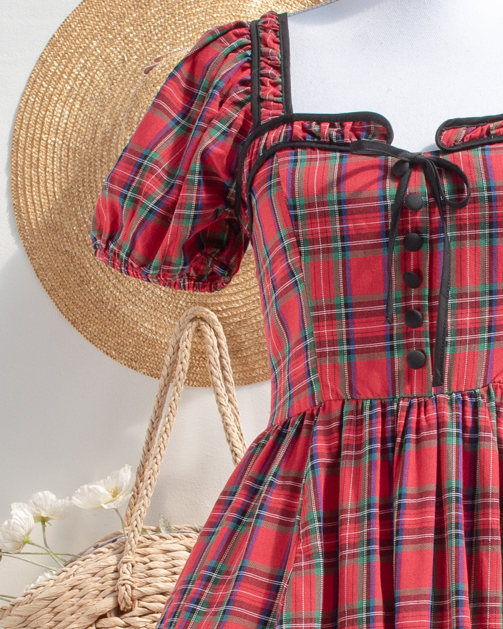 Red plaid cotton dress bodice with black piping, covered buttons, and a petite tie, front detail view.