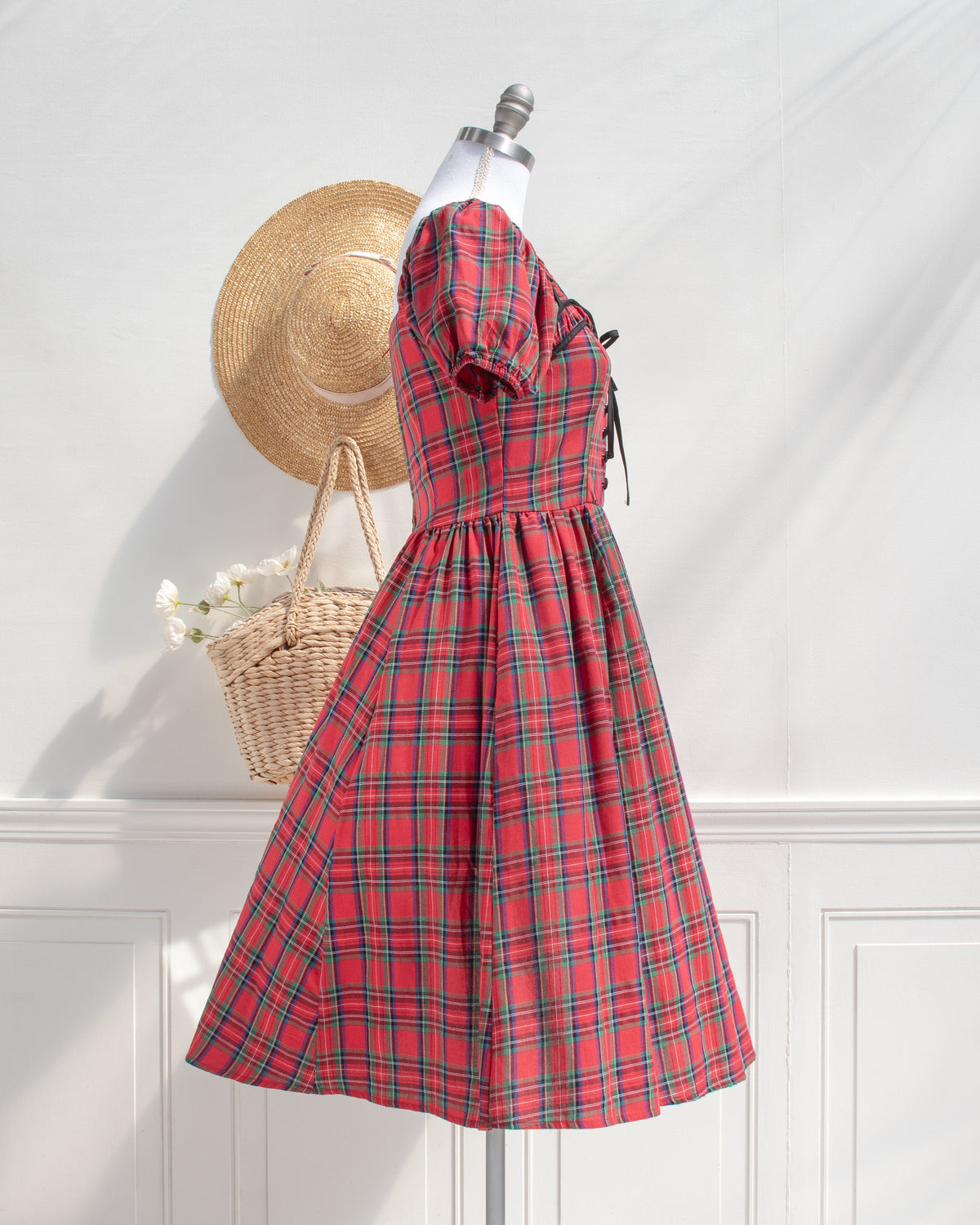 Red plaid cotton midi dress with a full swingy skirt and puff sleeves, styled with a woven basket, side view.