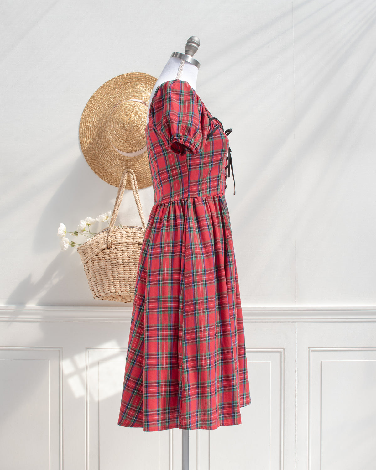 Red plaid cotton midi dress with puff sleeves and a fitted bodice, styled with a straw hat and basket, side view.