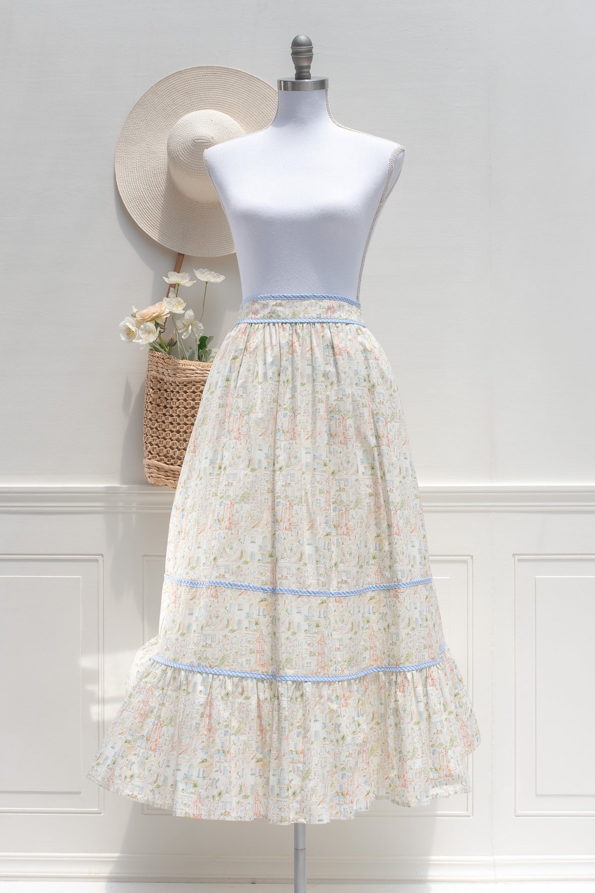 Cream retro village print cotton midi skirt with blue gingham trim and tiered ruffle hem, front view.