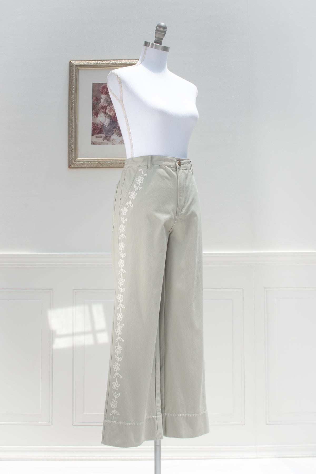 Sage cotton pants with white floral embroidery displayed on a mannequin, three quarter view.