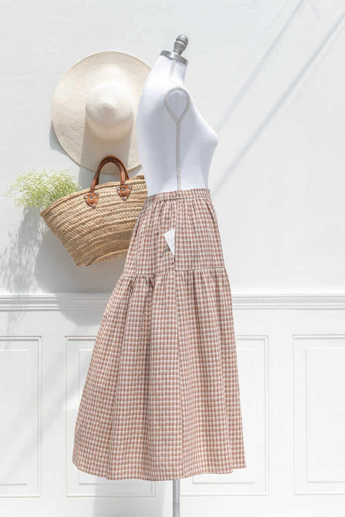 Mannequin wearing a white top and plaid skirt with a straw bag and hat on a white background