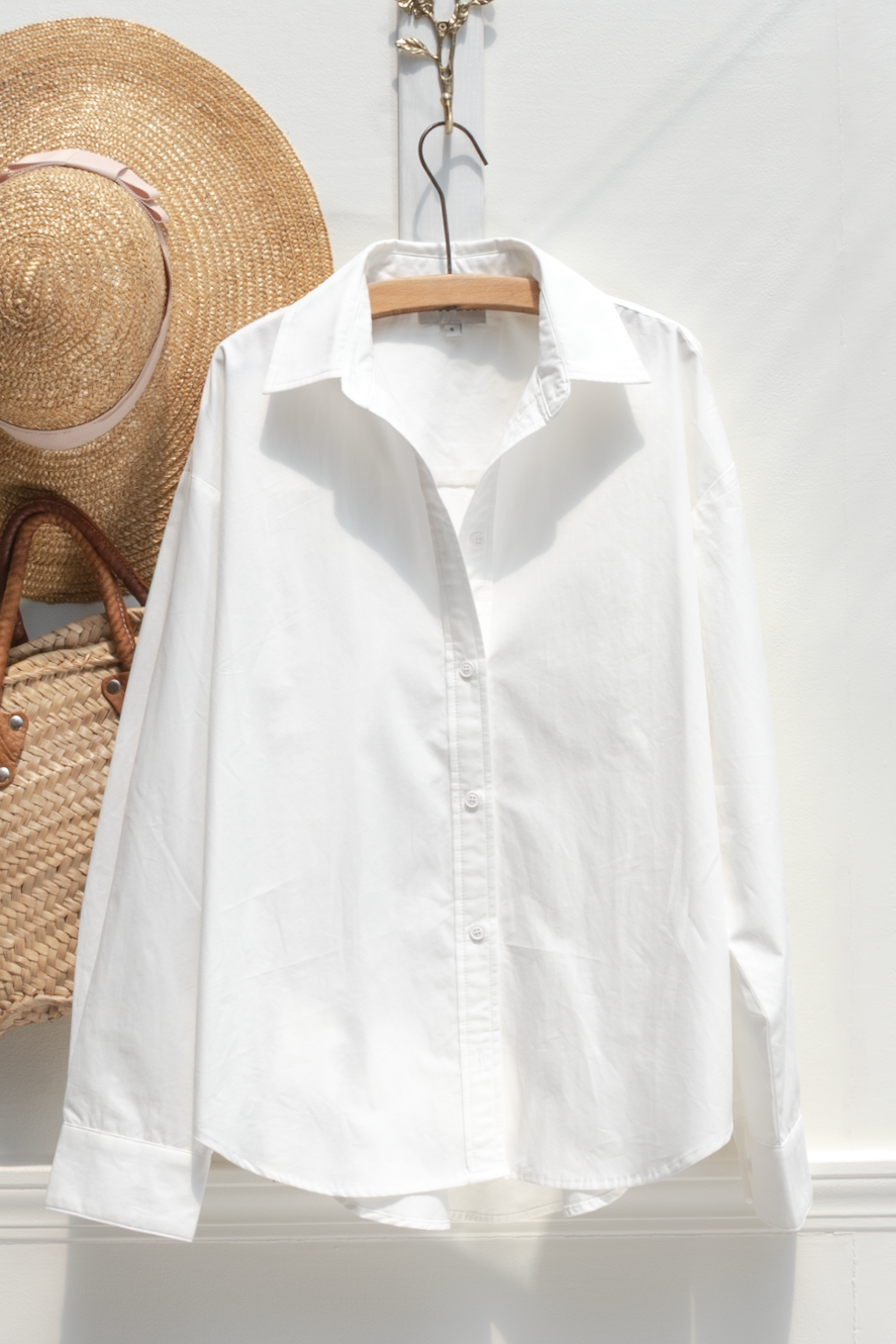 White cotton button up shirt shown on a hanger, front view.