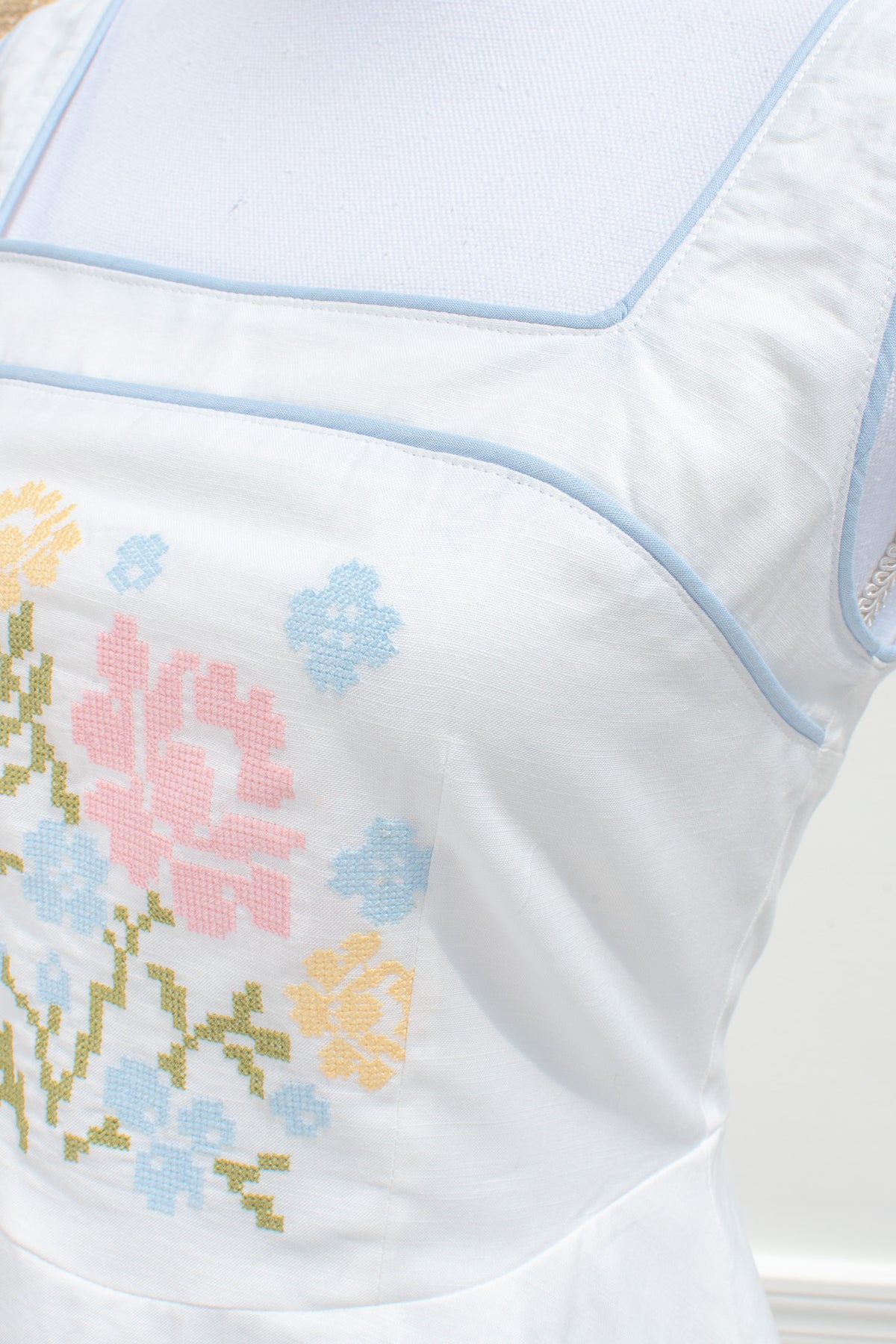 White cotton linen fabric with pink rose blue and yellow floral cross stitch embroidery close up.